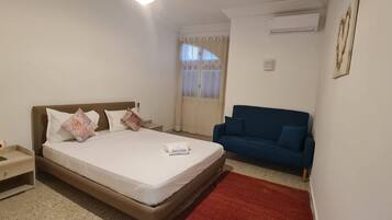 Una habitación de hotel con una cama individual, una mesita de noche, un sofá azul y una alfombra roja.