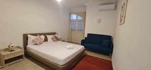 A hotel room with a single bed, a bedside table, a blue sofa, and a red rug. - Horizon Bleu Apartment With Sea View (La Marsa)