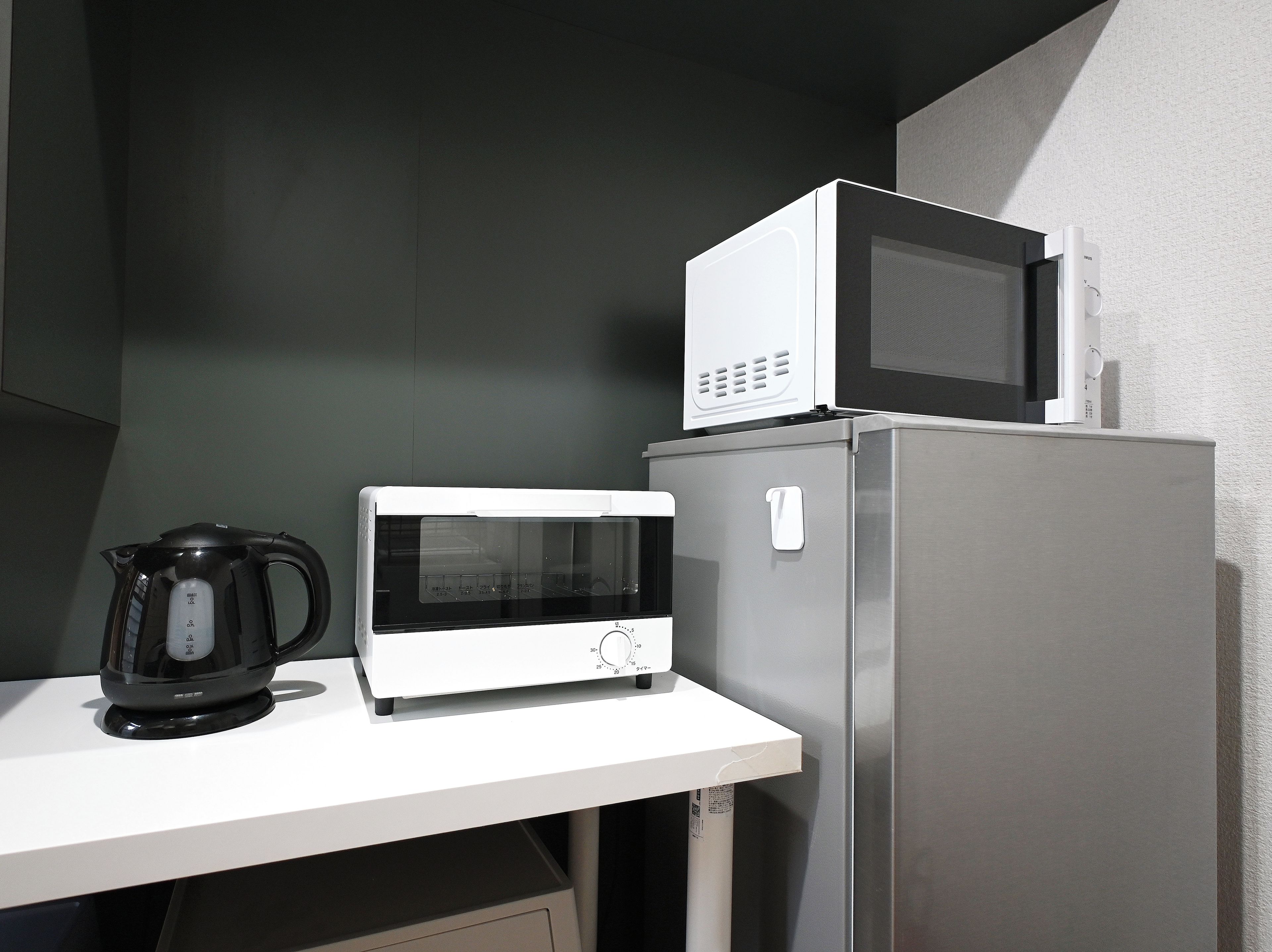 A kitchen with a microwave, a kettle, and a refrigerator.