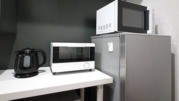 A kitchen with a microwave, a kettle, and a refrigerator.