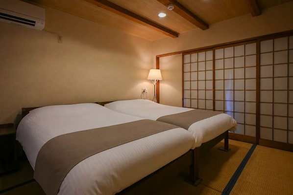 A hotel room with a traditional Japanese-style sliding door, a bed with a headboard, and a bedside lamp.