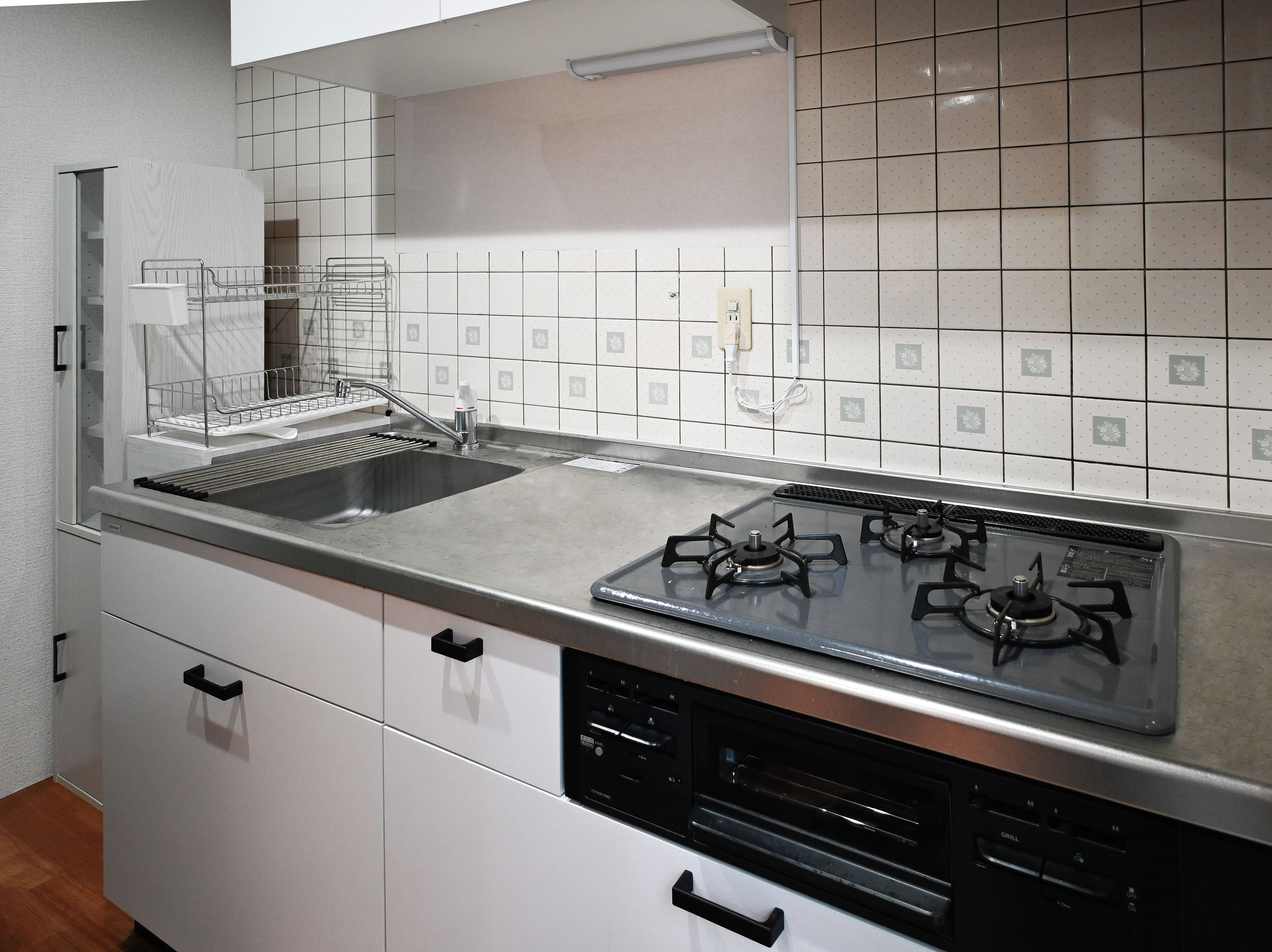 A kitchen with a stainless steel sink, a gas stove, and white cabinets.