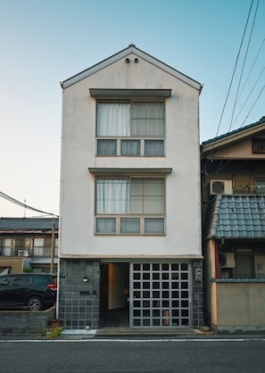 A two-story building with a flat roof, a garage entrance, and a visible satellite dish. - Common Table Okayama - 5 beds & 5 bikes (岡山市)