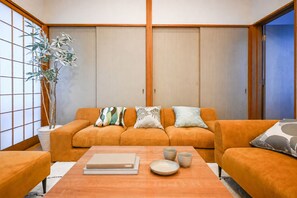A traditional Japanese-style room with a sofa set, cushions, a table with a book and bowls, and a potted plant.
