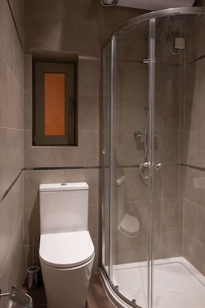 A bathroom with a toilet, a glass-enclosed shower, and a door with an orange frame. - Marea Grand Harbour  (Kalkara)