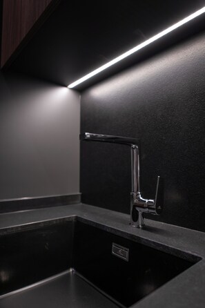 A modern kitchen with a sleek faucet, a black countertop, and under-cabinet lighting. - Marea Grand Harbour  (Kalkara)