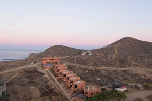 A coastal resort with multiple buildings, a dirt road, and a hilly landscape. - Cerritos Surf View (El Pescadero)