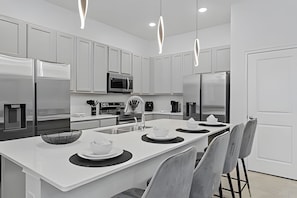 A modern kitchen with white cabinetry, stainless steel appliances, and a central island with bar seating. - 8BR Villa Avengers Game Room + Pool Disney (Orlando)