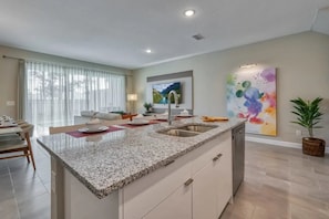 A modern kitchen with granite countertops, a built-in sink, and a dining area with a table and chairs. - Luxury 4BR Home With Private Pool (Kissimmee)