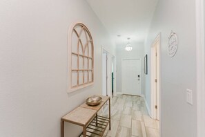A hallway with a wooden-framed window, a metal bowl on a table, and a door at the end. - 5-bedroom House With Private Pool (Kissimmee)