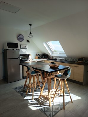 A modern kitchen with a skylight, a refrigerator, a microwave, and a dining area with chairs and a table. - Apartment in a typical village in Finistère. (Plogoff)