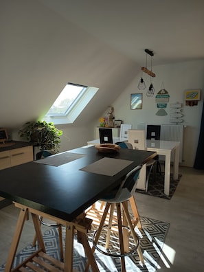 A modern loft bedroom with a skylight, a dining area with a black table, and a workspace with a computer. - Apartment in a typical village in Finistère. (Plogoff)