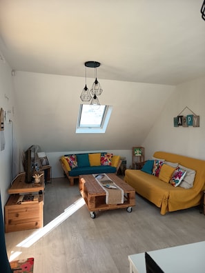 Een knus loft-stijl woongedeelte met een bank, salontafel en een televisie op een houten standaard.