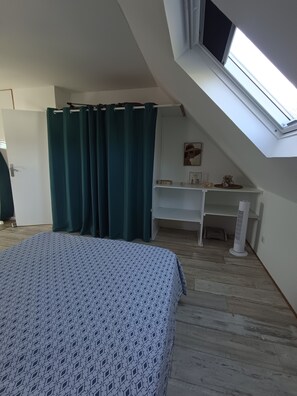A bedroom with a bed, a desk, a standing fan, and a skylight. - Apartment in a typical village in Finistère. (Plogoff)