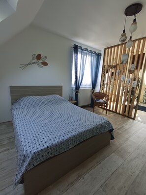 Een slaapkamer met een bed, een stoel, een raam met gordijnen, een radiator en een decoratie aan de muur.