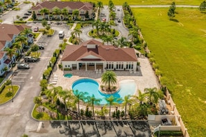 An aerial view of a residential area with a large swimming pool surrounded by palm trees and a clubhouse. - Stylish 4BR Townhome 10 Min to Disney (Kissimmee)