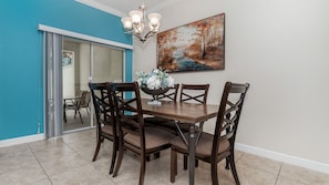 A dining area with a wooden table and chairs, a chandelier, and a painting on the wall. - Storey Lake 10 mim -> Disney 4bd/3ba (Kissimmee)