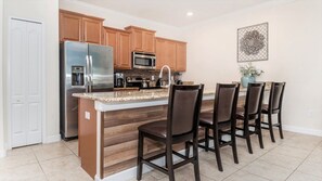 A kitchen with wooden cabinets, stainless steel appliances, a granite countertop, and a dining area with four chairs. - Storey Lake 10 mim -> Disney 4bd/3ba (Kissimmee)