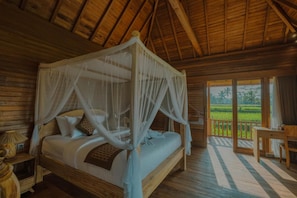 A wooden four-poster bed with a canopy, a nightstand, and a view of a lush landscape through a glass door. - Villa Suda Ubud by Dhananjaya (Ubud)
