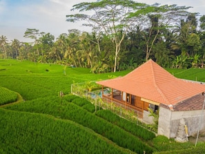 A house with a tiled roof surrounded by lush green fields and trees. - Villa Suda Ubud by Dhananjaya (Ubud)