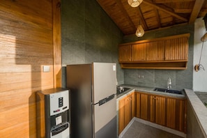 A compact kitchen with a built-in refrigerator, a water dispenser, and wooden cabinets. - Villa Suda Ubud by Dhananjaya (Ubud)