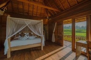 A wooden four-poster bed with a canopy, a wooden desk, and a view of a green landscape through an open door. - Villa Suda Ubud by Dhananjaya (Ubud)