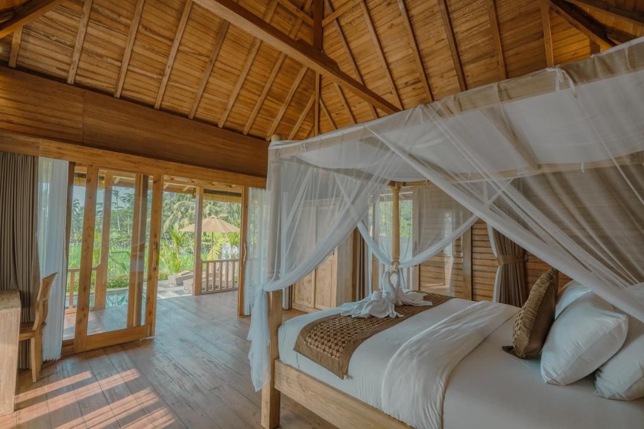 Een kamer met houten frame, een bed onder een hemelbed, grote ramen en uitzicht op groen buiten.