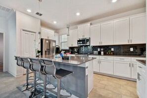 A modern kitchen with white cabinets, stainless steel appliances, and a bar area with stools. - 5BR Storey Lake Home, Pool & Game Room (Kissimmee)