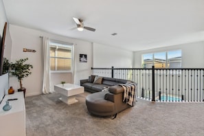 A modern living room with a sectional sofa, a white coffee table, and a ceiling fan. A balcony with a pool is visible through the railing. - 5BR Storey Lake Home, Pool & Game Room (Kissimmee)