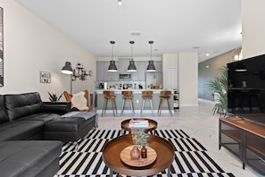 Un salon moderne avec un canapé en cuir noir, un tapis à rayures et une table basse en bois agrémentée de vases.