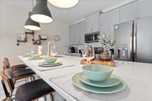 Une cuisine moderne dotée d’un îlot central, de luminaires suspendus et d’appareils électroménagers en acier inoxydable.