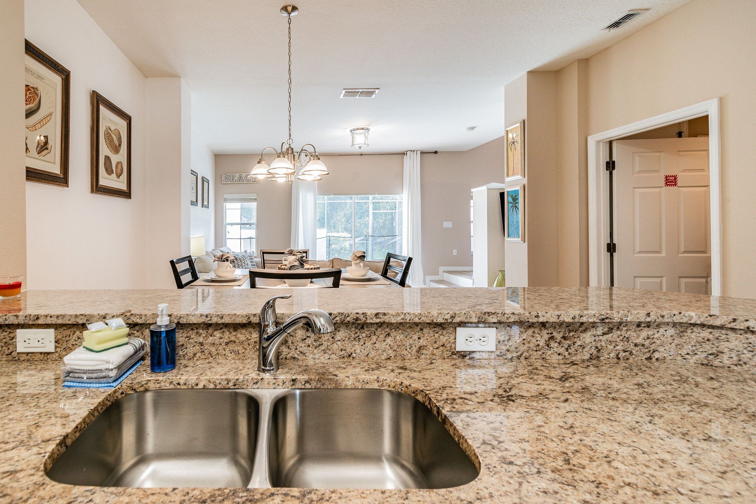 A kitchen with granite countertops, stainless steel sink, and pendant lighting.