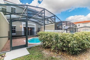 A modern building with a glass-enclosed patio area, a swimming pool, and a well-maintained hedge. - 3BR Bella Vida Pool Home by Walmart (Kissimmee)