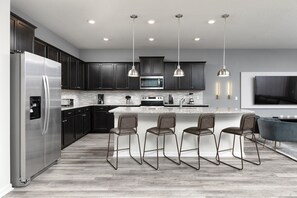 A modern kitchen with dark cabinets, stainless steel appliances, and a central island with bar stools. - 10 Bedrooms / 8 Bathrooms - Windsor Island Resort (Davenport)