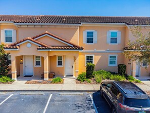 A row of townhouses with a tiled roof, numbered doors, and a parking lot in front. - 2BR Regal Oaks Townhome With Jacuzzi (Kissimmee)