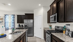 A modern kitchen with dark wood cabinets, stainless steel appliances, granite countertops, and a built-in microwave. - 5BR Villa w/ Pool + Resort Access Solterra (Davenport)