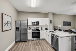 Een moderne keuken met roestvrijstalen apparatuur, witte kastjes en een houten vloer.