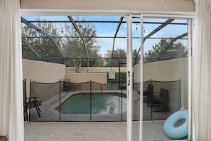 An outdoor pool area with a glass enclosure, a pool, and seating. - Windsor Hills 3BR Home w/ Pool Near Disney (Kissimmee)