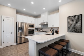 A modern kitchen with white cabinets, stainless steel appliances, and a central island with bar stools. - Reunion 4BR Luxury Villa PS5 + Game Room (Kissimmee)