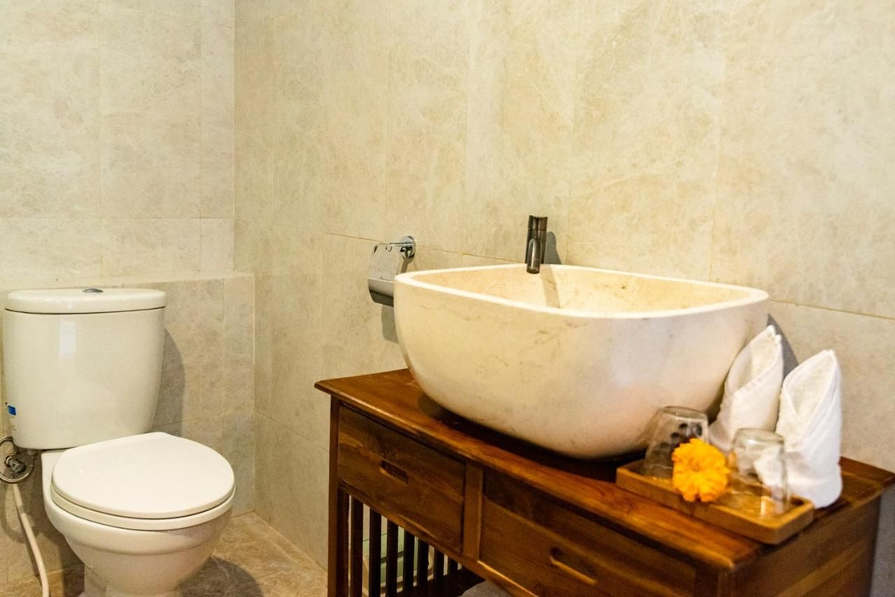 A bathroom with a toilet, a large vessel sink, and a wooden vanity with a towel and a flower.
