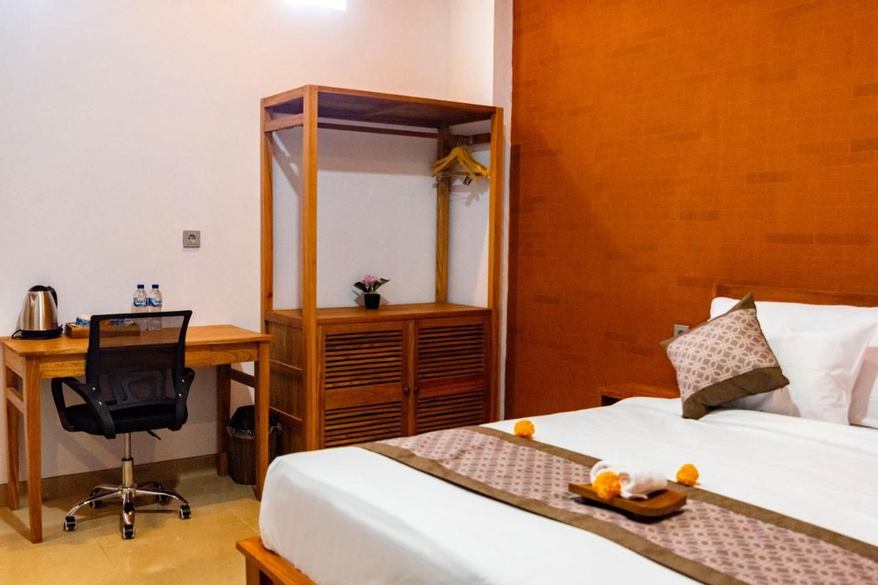 A hotel room with a bed, a desk with a chair, a wardrobe, and a small table with fruit.