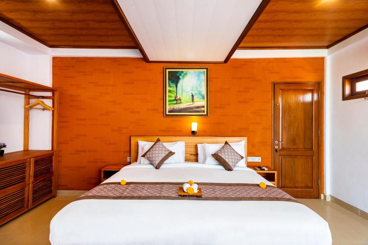 Habitación de hotel con una cama grande, cabecero de madera, un cuadro sobre la cama, armario de madera y una puerta.