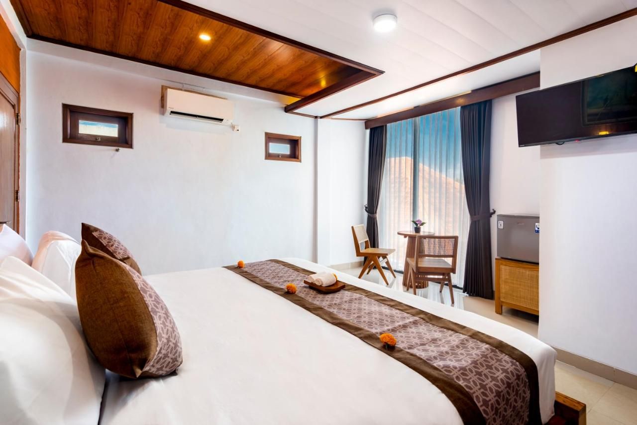 Una habitación de hotel con cama, escritorio, silla, televisión y ventana con cortinas.