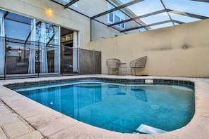 A swimming pool with a glass enclosure, a covered patio area, and a view of a building with large windows. - Windsor Hills 3BR Pool,8min to Disney & Water Park (Kissimmee)