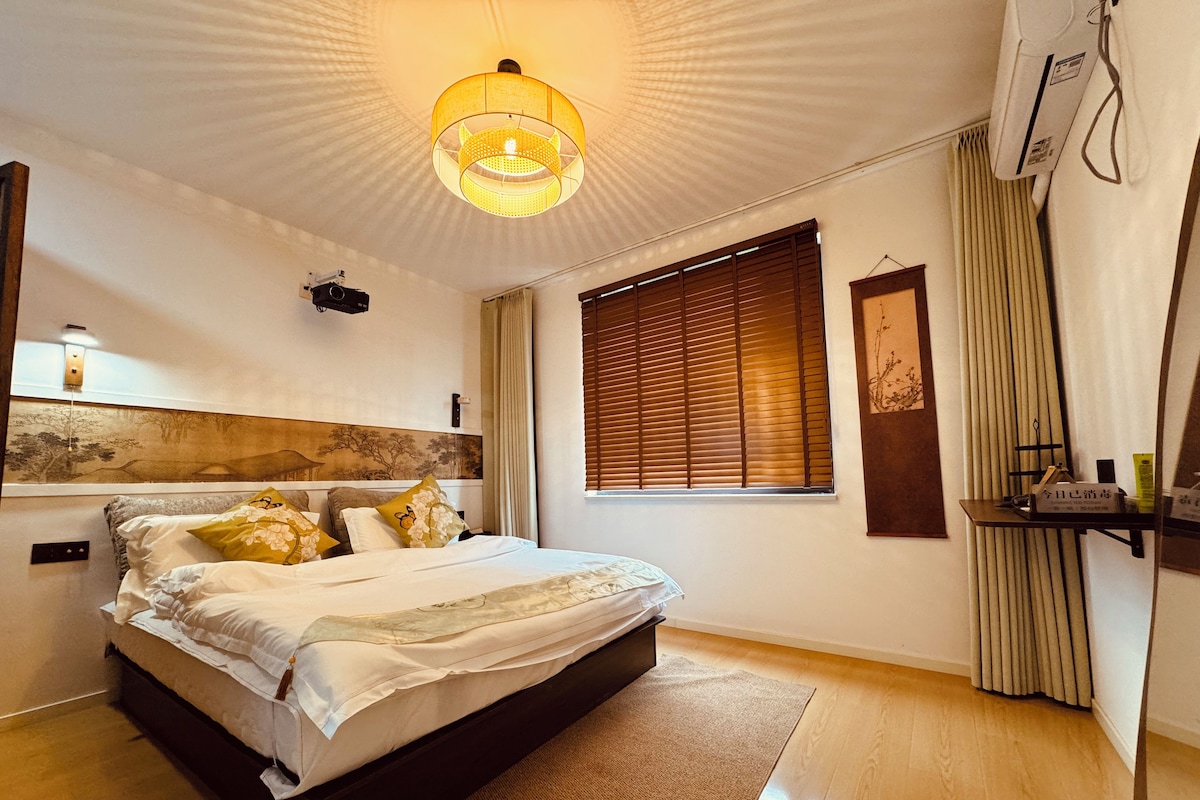 Et moderne soveværelse med en stor seng, en loftlampe, et vindue med persienner og et sengebord.