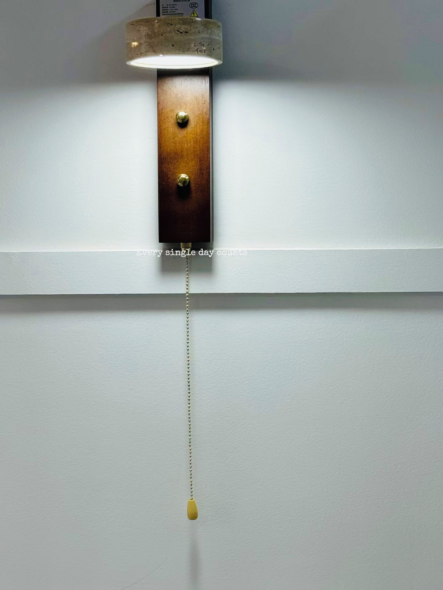 A wall-mounted light fixture with a wooden base and a hanging pendant.