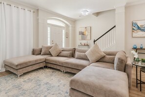 A beige sectional sofa with a matching ottoman, a small side table, and a staircase with a railing. - Windsor Hills 6BR Villa w/ Pool & Game Room (Kissimmee)