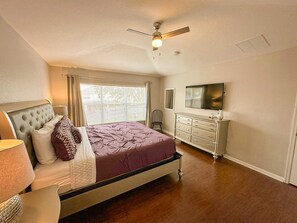 A bedroom with a bed, a dresser, a ceiling fan, a window with blinds, and a television on the wall. - Windsor Hills 6BR Villa w/ Pool & Game Room (Kissimmee)