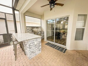 A patio area with a stone countertop, a grill, and a ceiling fan. - Windsor Hills 6BR Villa w/ Pool & Game Room (Kissimmee)