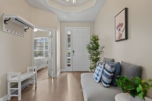 Een moderne woonkamer met een bank, een witte hocker, een potplant en een deur naar een andere kamer.